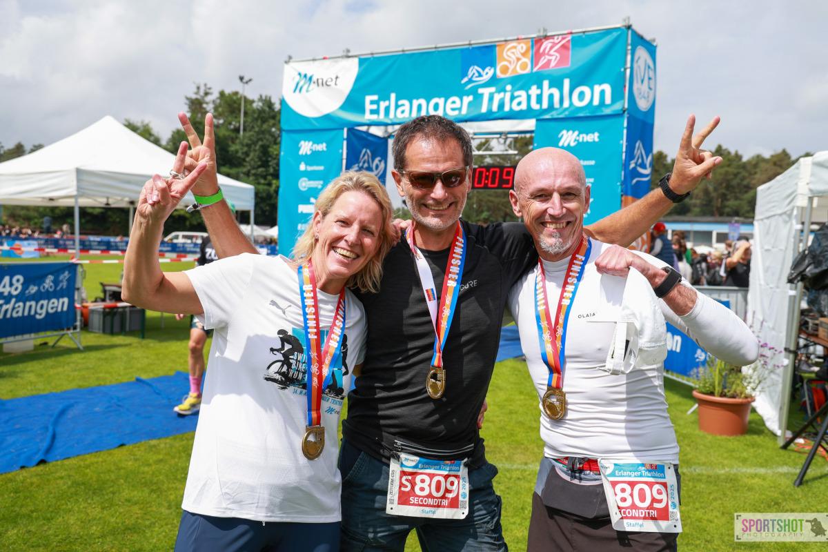 Foto vom 3 Personen mit Finishermedallien vor dem Zielbogen des Erlanger Triathlon