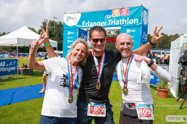 Foto vom 3 Personen mit Finishermedallien vor dem Zielbogen des Erlanger Triathlon