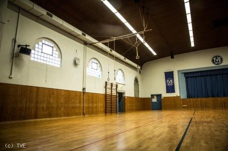 Innenansicht der Jahnhalle mit Holzfußboden, Turngeräten und großen Fenstern.