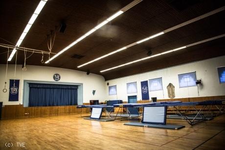 Innenansicht der Jahnhalle mit mehreren aufgebauten Trampolinen und Turnringen.