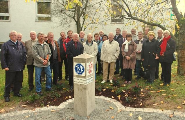 Fusion TV48 und FC West Eine Gruppe Menschen steht versammelt um eine kleine Säule mit den Logos von TV 1848 Erlangen und 1. FC Erlangen-West.