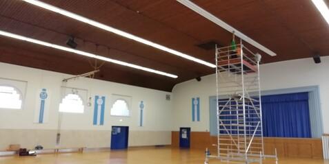 Eine Person montiert eine neue Beleuchtung in der Haupthalle der Jahnhalle auf einem Ger&uuml;st.