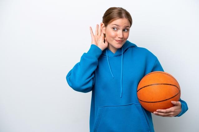 Eine sportliche Frau lauscht den Geräuschen und hält einen Basketball in der Hand.