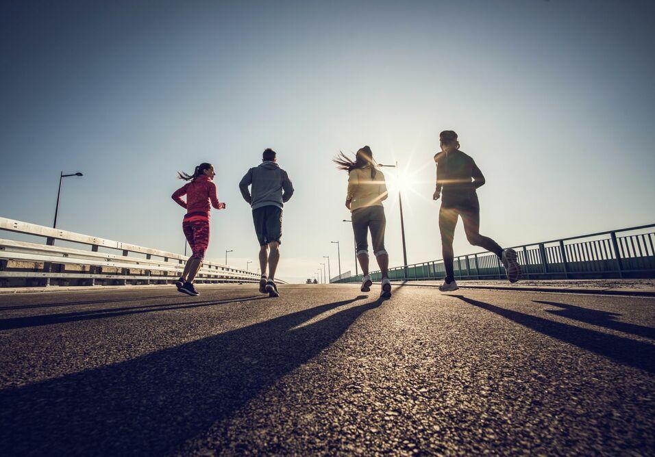 Joggen auf einer Brücke Vier Personen joggen auf einer Brücke bei tiefstehender Sonne.