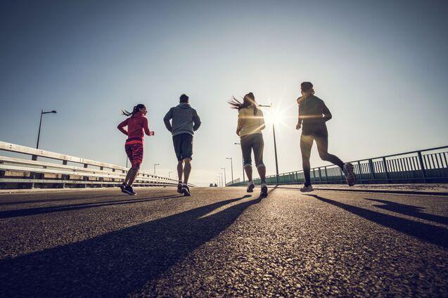 Vier Personen joggen auf einer Brücke bei tiefstehender Sonne.