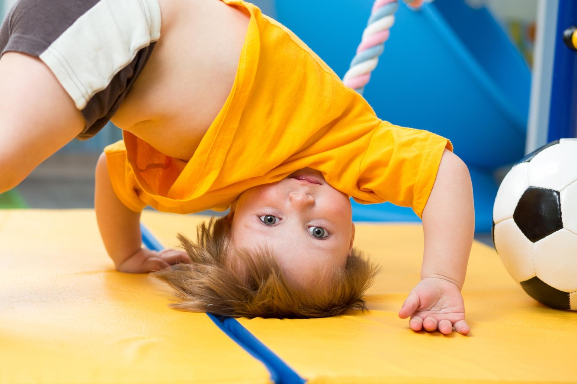 Kind beim Turnen Ein Kind macht einen Handstand auf einer gelben Turnmatte, neben einem Fußball.
