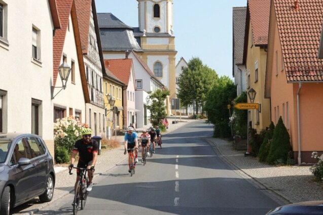 Foto: Bergabfahrende Rennradfahrer zwischen Häusern