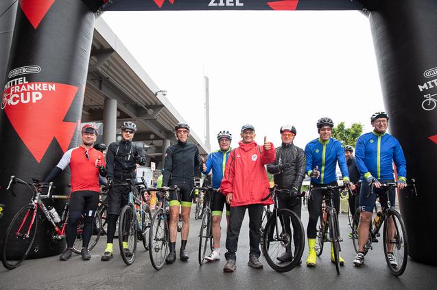Gruppenfoto vieler Personen mit Rennr&auml;dern unter dem RTF-Startbogen